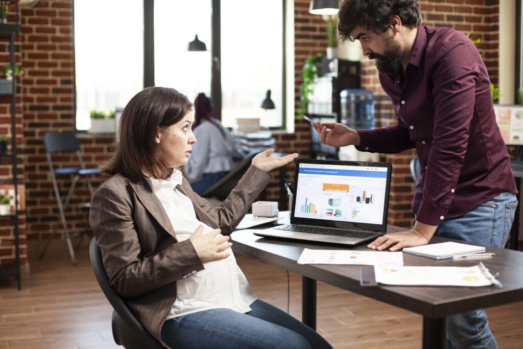Two coworkers discussing data on a laptop in a modern office setting.